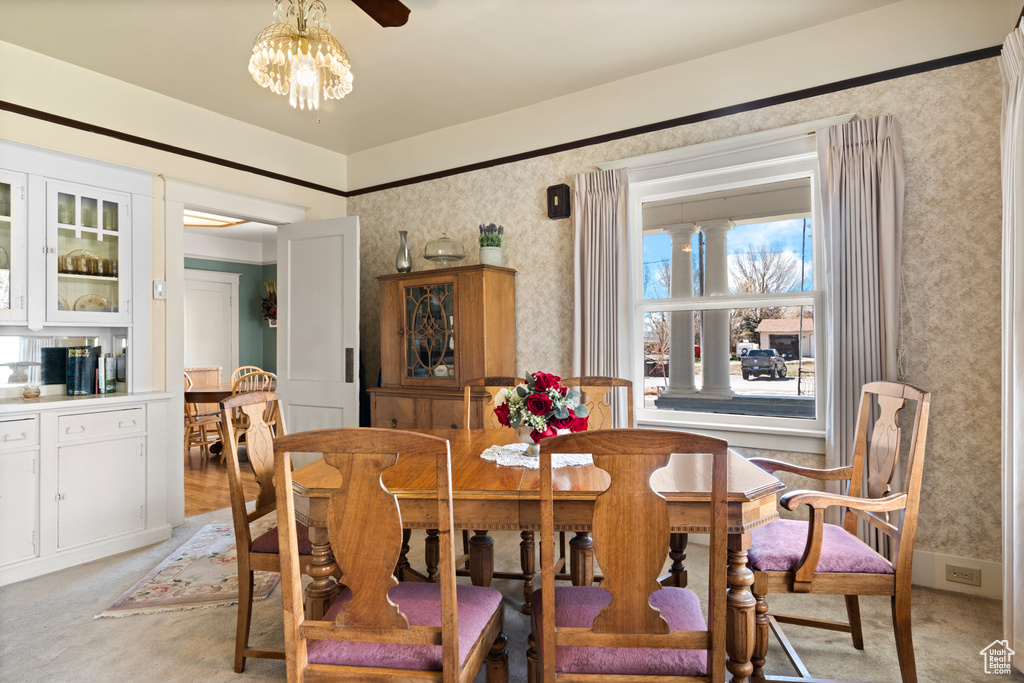 Dining space with light carpet, a notable chandelier, and wallpapered walls