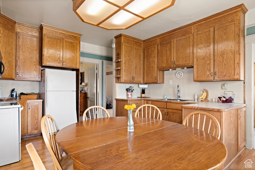 Kitchen with freestanding refrigerator, brown cabinetry, stove, light wood finished floors, and a sink
