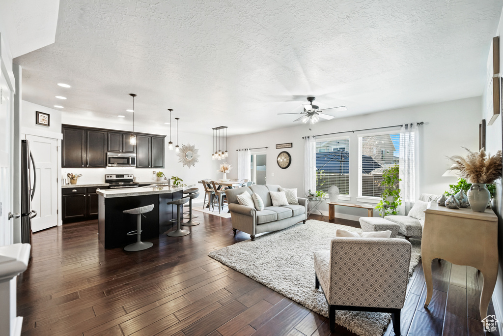 Living room featuring a textured ceiling, dark wood finished floors, recessed lighting, a ceiling fan, and baseboards