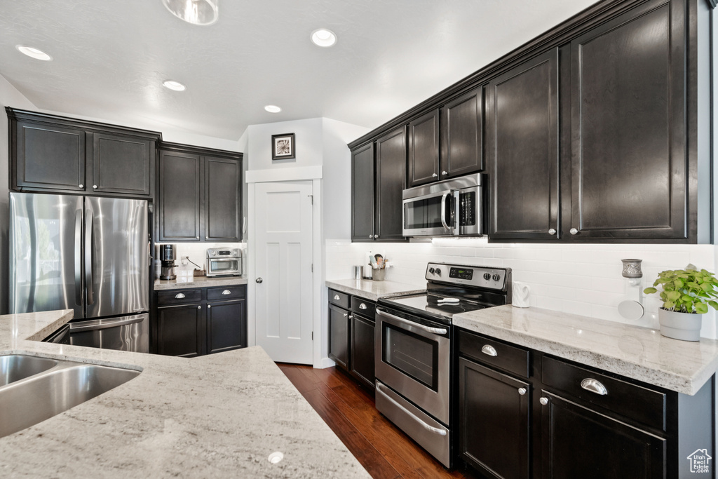 Kitchen with stainless steel appliances, dark wood-style flooring, light stone countertops, backsplash, and recessed lighting