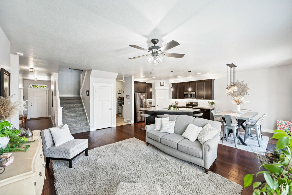 Living room with dark wood-style flooring, stairs, baseboards, and a ceiling fan