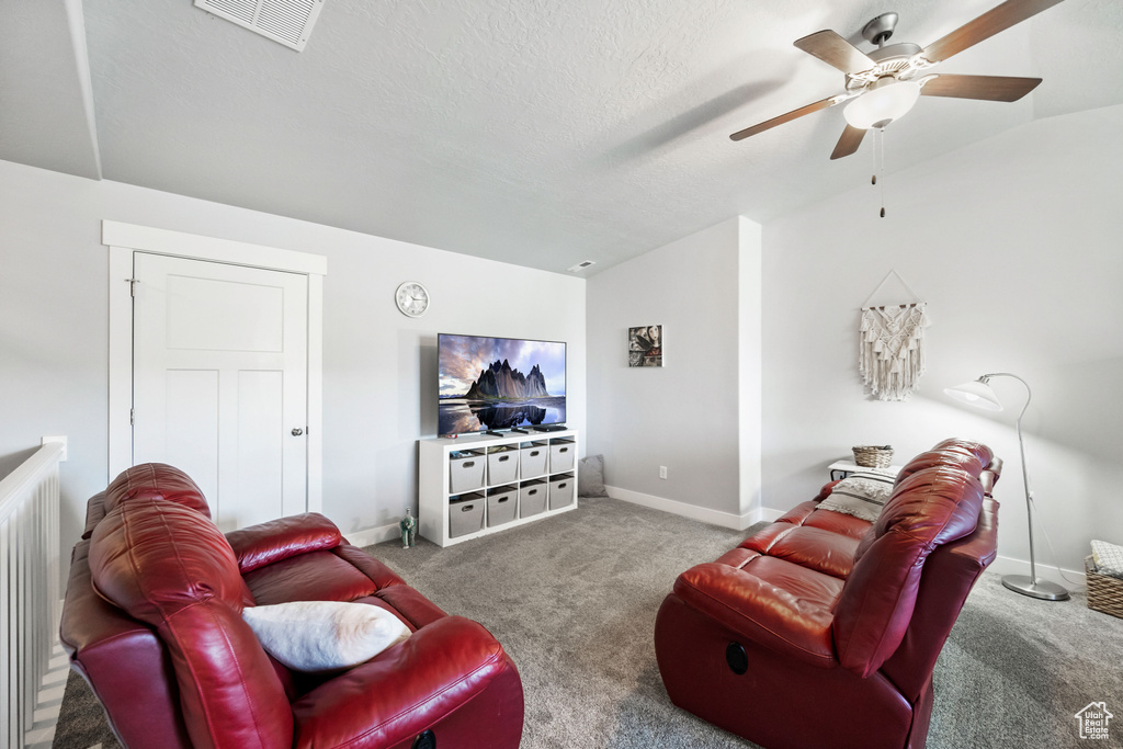 Carpeted living area featuring vaulted ceiling, baseboards, visible vents, and ceiling fan