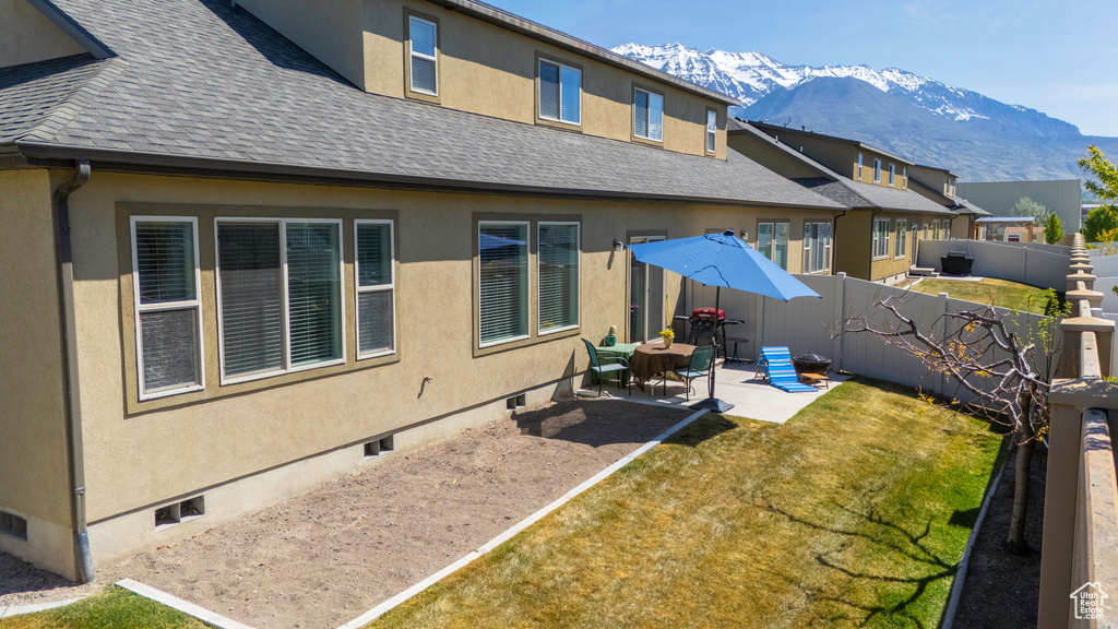 Rear view of house featuring a mountain view, a patio, a lawn, a shingled roof, and a fenced backyard