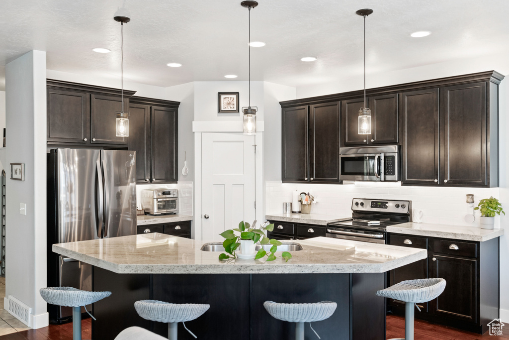Kitchen with stainless steel appliances, tasteful backsplash, a kitchen bar, and dark brown cabinets