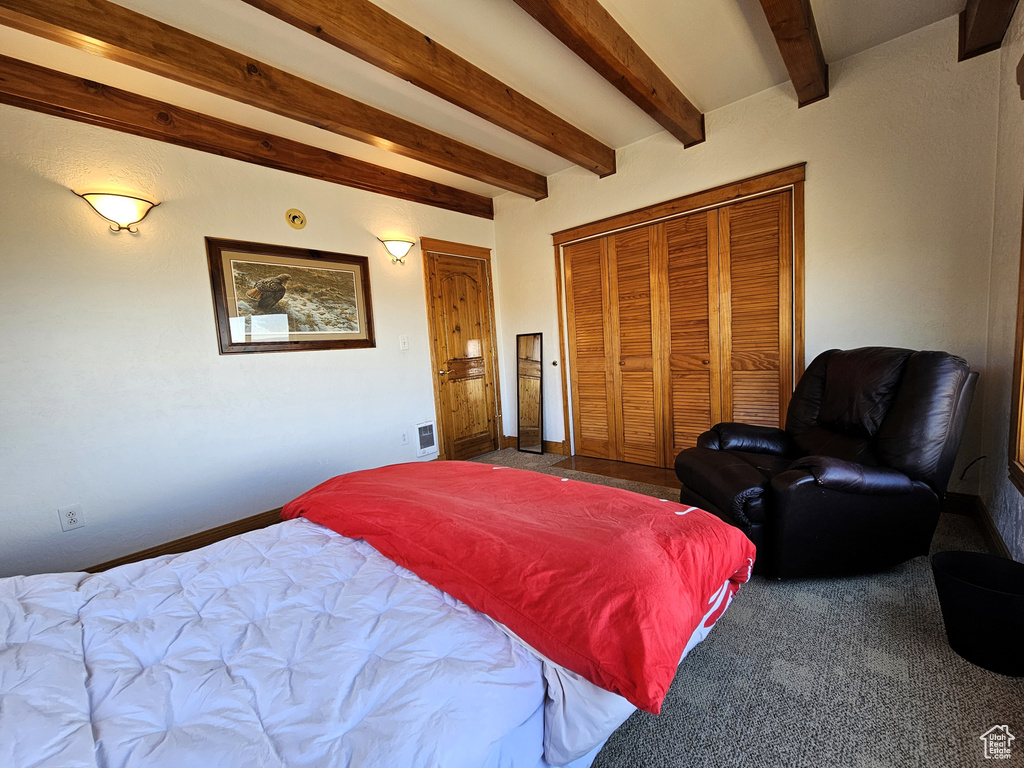 Carpeted bedroom with a closet, baseboards, and beamed ceiling