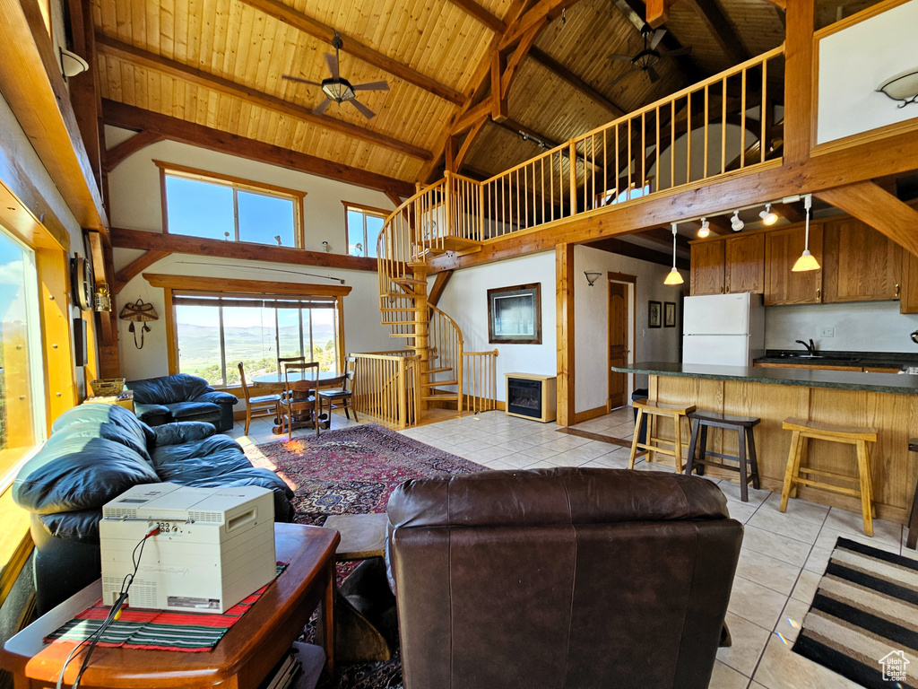 Living room with a ceiling fan, light tile patterned flooring, wood ceiling, stairs, and high vaulted ceiling
