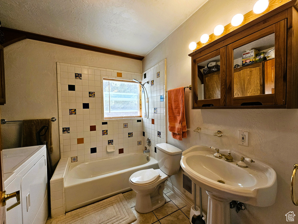 Bathroom with a textured ceiling, toilet, tile patterned flooring, shower / washtub combination, and washing machine and clothes dryer