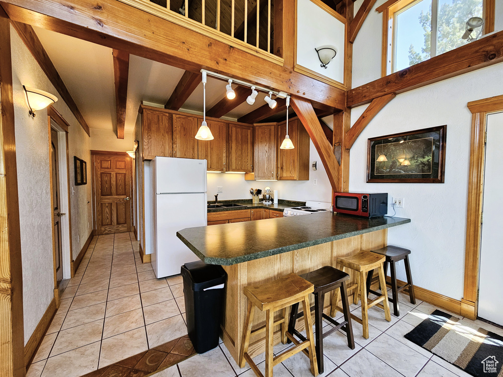 Kitchen featuring a peninsula, light tile patterned floors, freestanding refrigerator, dark countertops, and beam ceiling