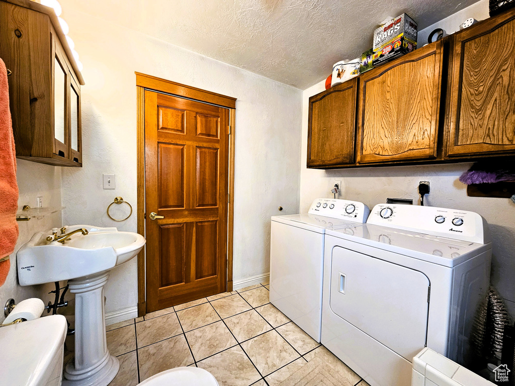 Laundry room featuring a textured ceiling, light tile patterned flooring, cabinet space, and washer and dryer