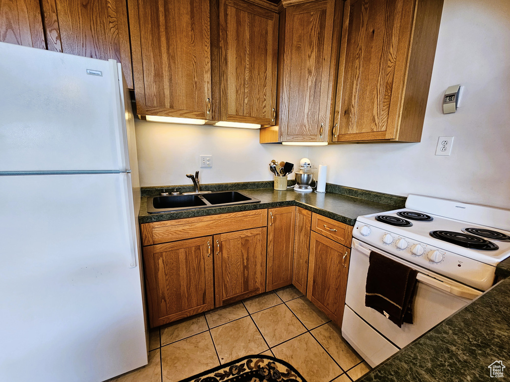 Kitchen with light tile patterned floors, white appliances, a sink, brown cabinets, and dark countertops