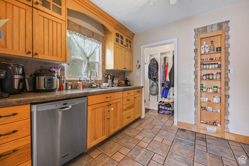Kitchen featuring stainless steel dishwasher, a sink, decorative backsplash, stone finish flooring, and dark countertops