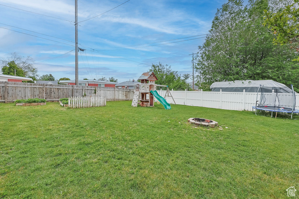 View of yard with a trampoline, a playground, and an outdoor fire pit