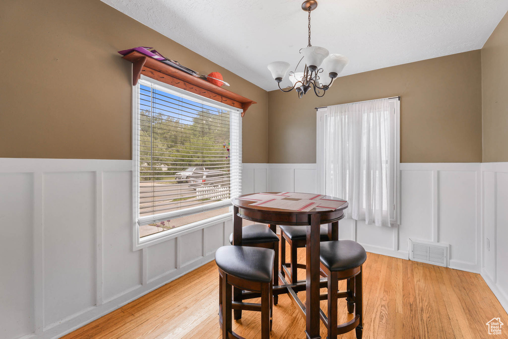 Dining room featuring a decorative wall, a chandelier, a wainscoted wall, and light wood-style floors