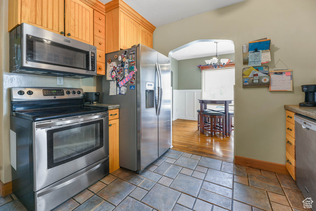 Kitchen featuring stainless steel appliances, a chandelier, stone tile floors, arched walkways, and baseboards