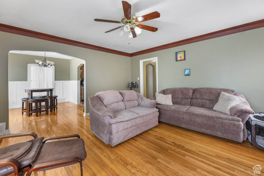 Living area featuring light wood finished floors, a chandelier, ceiling fan, arched walkways, and ornamental molding
