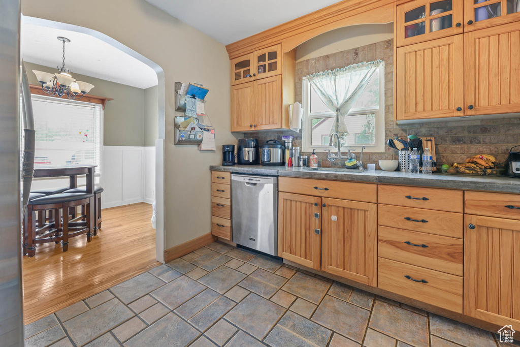 Kitchen with stainless steel dishwasher, a sink, a chandelier, dark countertops, and a wainscoted wall