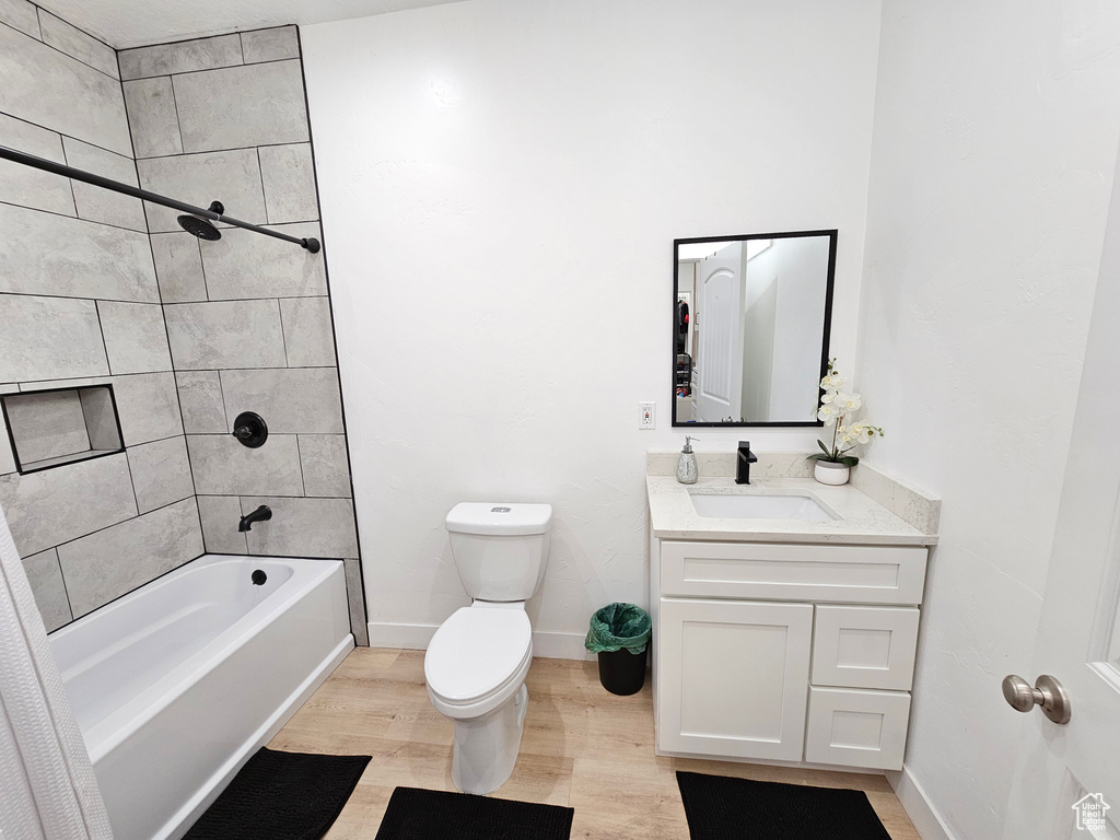 Full bathroom with vanity, wood finished floors, toilet, baseboards, and shower / tub combination