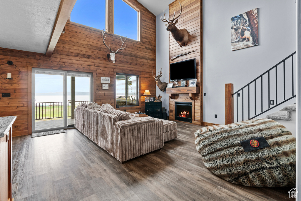 Living area with wood walls, stairs, wood finished floors, a high ceiling, and a stone fireplace