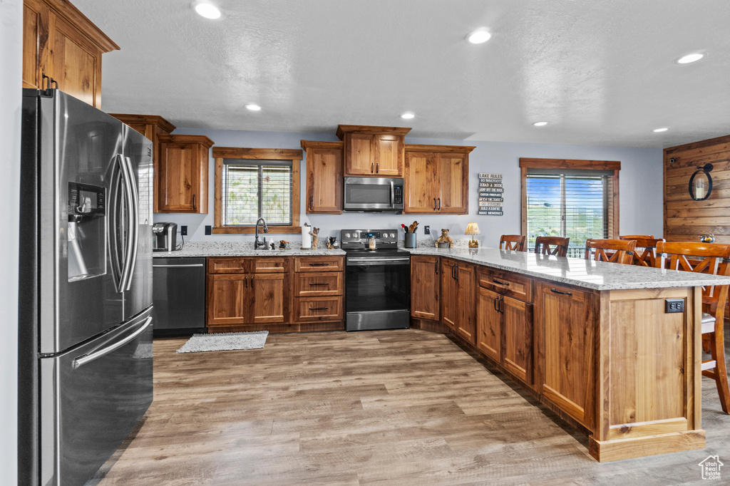 Kitchen featuring a sink, a peninsula, brown cabinetry, and appliances with stainless steel finishes