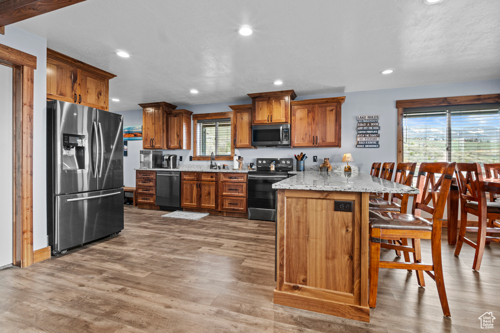 Kitchen featuring brown cabinetry, stainless steel appliances, a kitchen bar, and light wood-type flooring