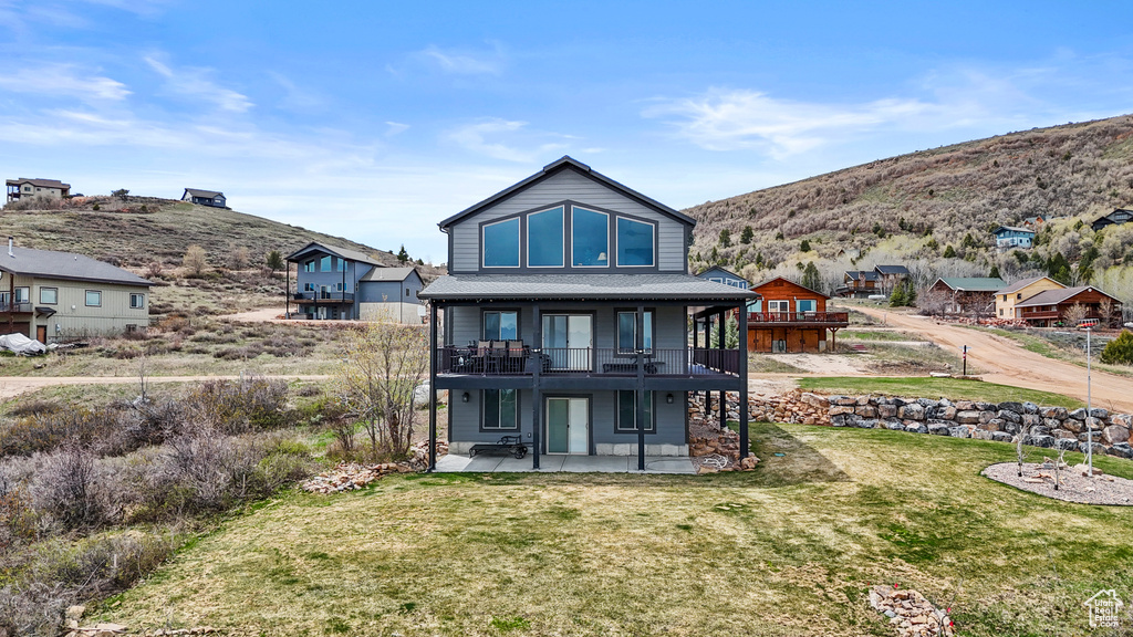Rear view of house featuring a yard, a patio area, roof with shingles, and a deck with mountain view