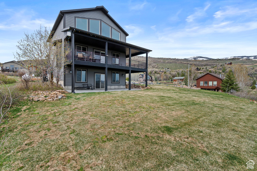 Back of property featuring a balcony, a yard, a patio, and a mountain view