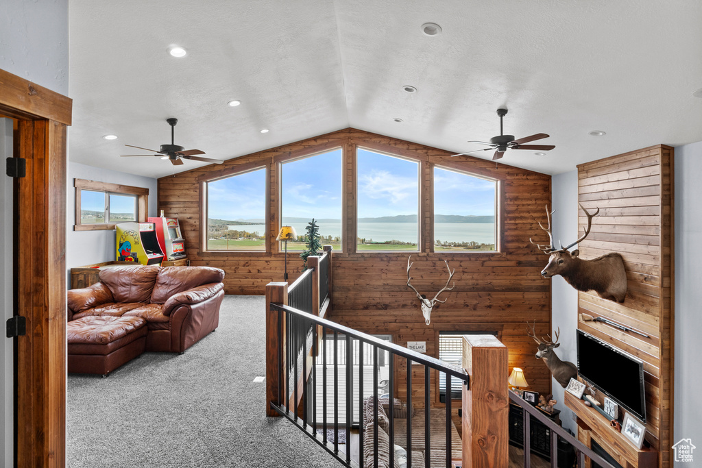 Carpeted living area featuring vaulted ceiling, wooden walls, a ceiling fan, and recessed lighting