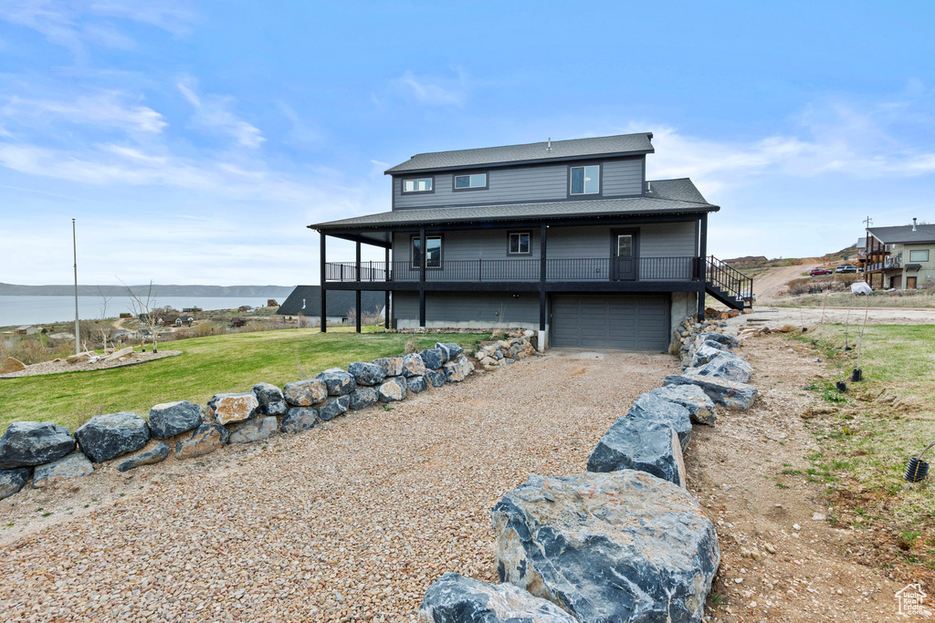 Back of house featuring a lawn, driveway, a garage, a water view, and stairs