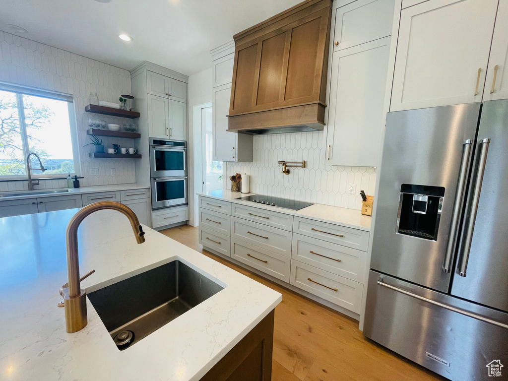 Kitchen with a sink, custom exhaust hood, stainless steel appliances, and backsplash