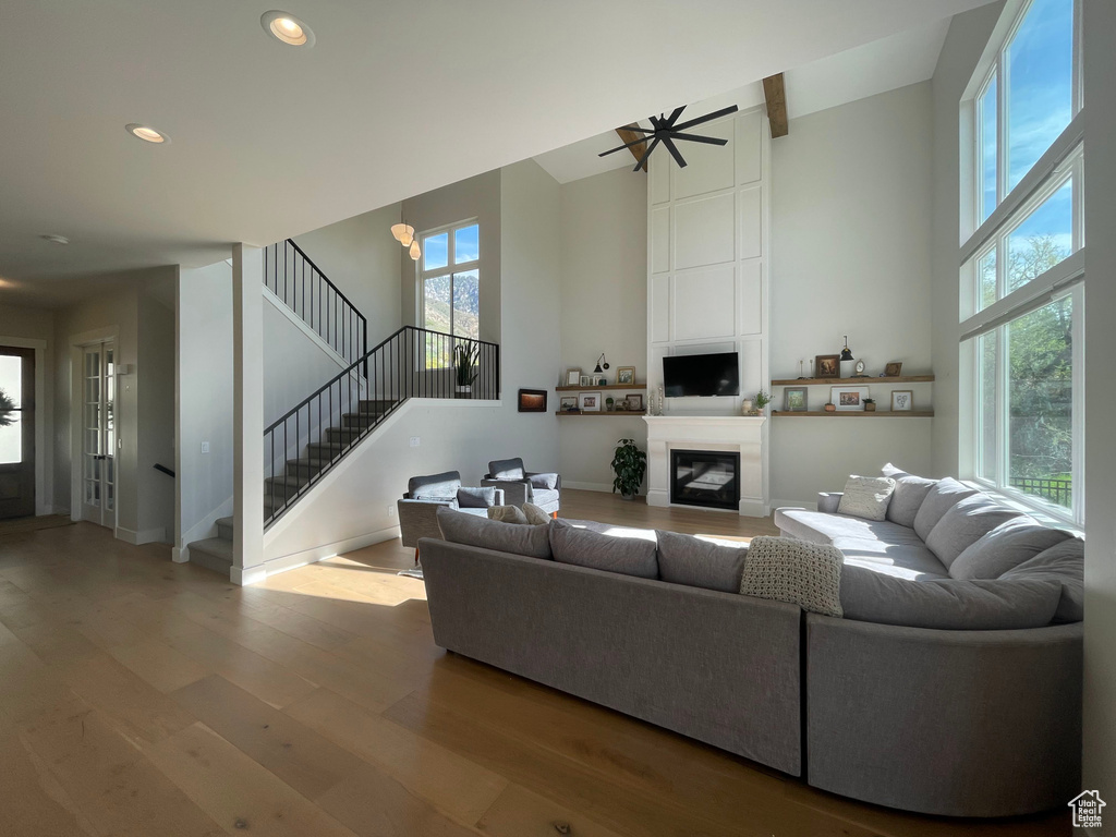 Living room with a large fireplace, wood finished floors, stairway, a high ceiling, and recessed lighting
