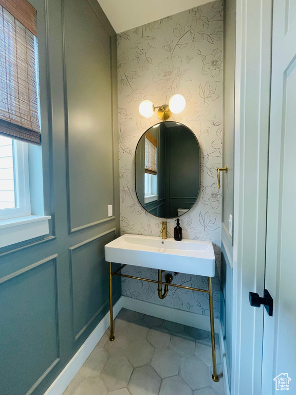 Bathroom with wallpapered walls, a sink, tile patterned floors, and baseboards