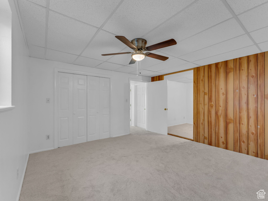 Unfurnished bedroom featuring a paneled ceiling, wood walls, carpet, and a ceiling fan