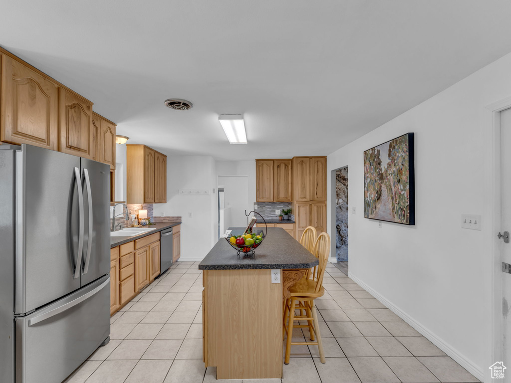 Kitchen featuring a sink, stainless steel appliances, tasteful backsplash, a kitchen bar, and light tile patterned floors