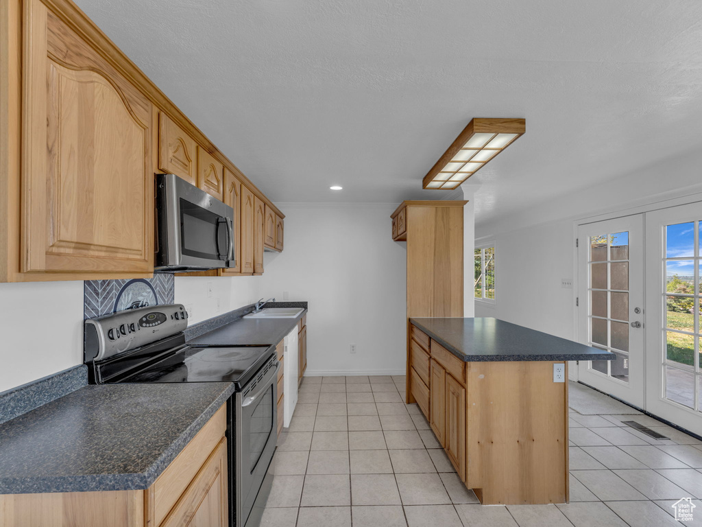 Kitchen with dark countertops, appliances with stainless steel finishes, light tile patterned floors, and a healthy amount of sunlight