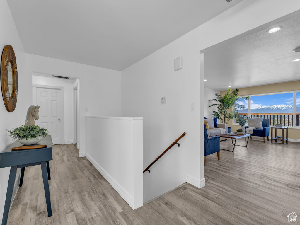 Hallway with light wood finished floors, baseboards, and an upstairs landing