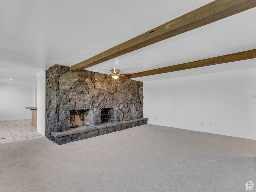 Unfurnished living room featuring carpet, tile patterned floors, ceiling fan, beamed ceiling, and a stone fireplace