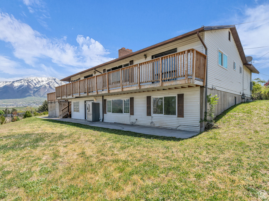 Back of property with a patio area, a deck with mountain view, and a lawn