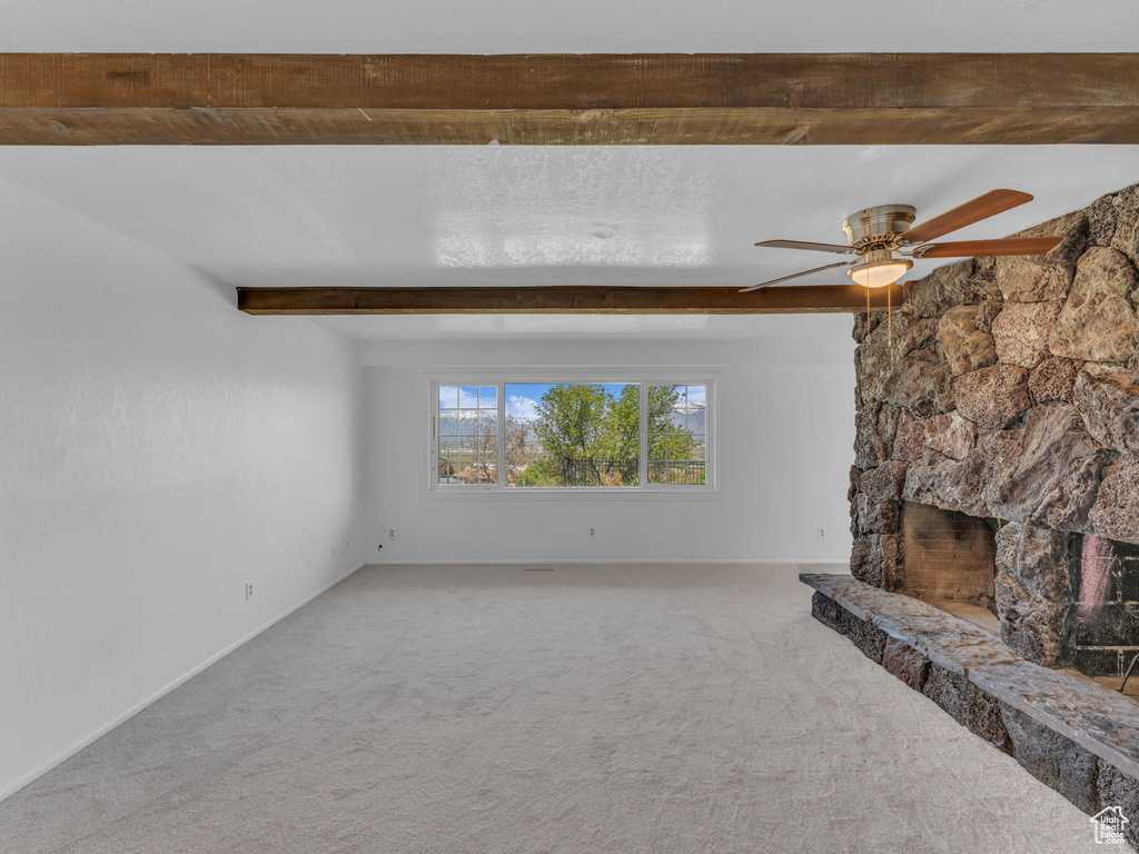 Unfurnished living room with a ceiling fan, beamed ceiling, and carpet floors