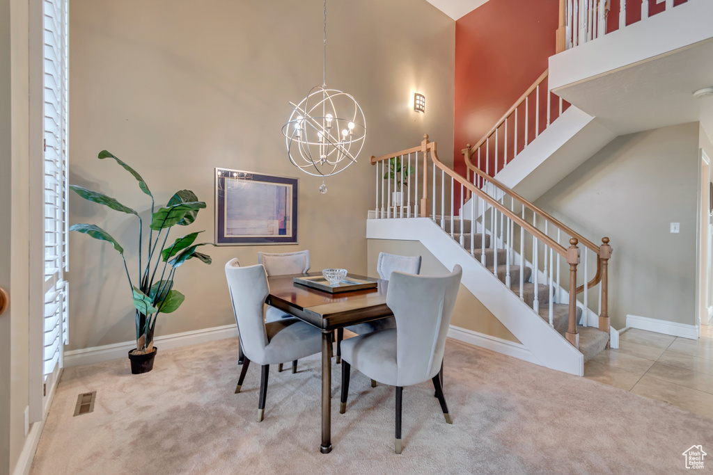 Carpeted dining area featuring baseboards, an inviting chandelier, visible vents, a towering ceiling, and stairway