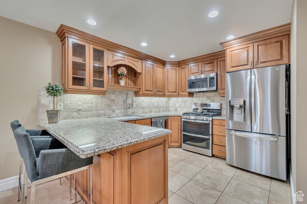 Kitchen featuring a peninsula, glass insert cabinets, a sink, stainless steel appliances, and decorative backsplash