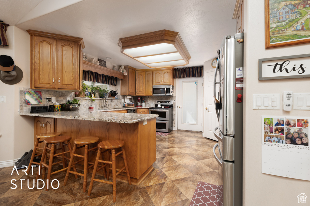Kitchen featuring light stone counters, a kitchen breakfast bar, a peninsula, decorative backsplash, and appliances with stainless steel finishes