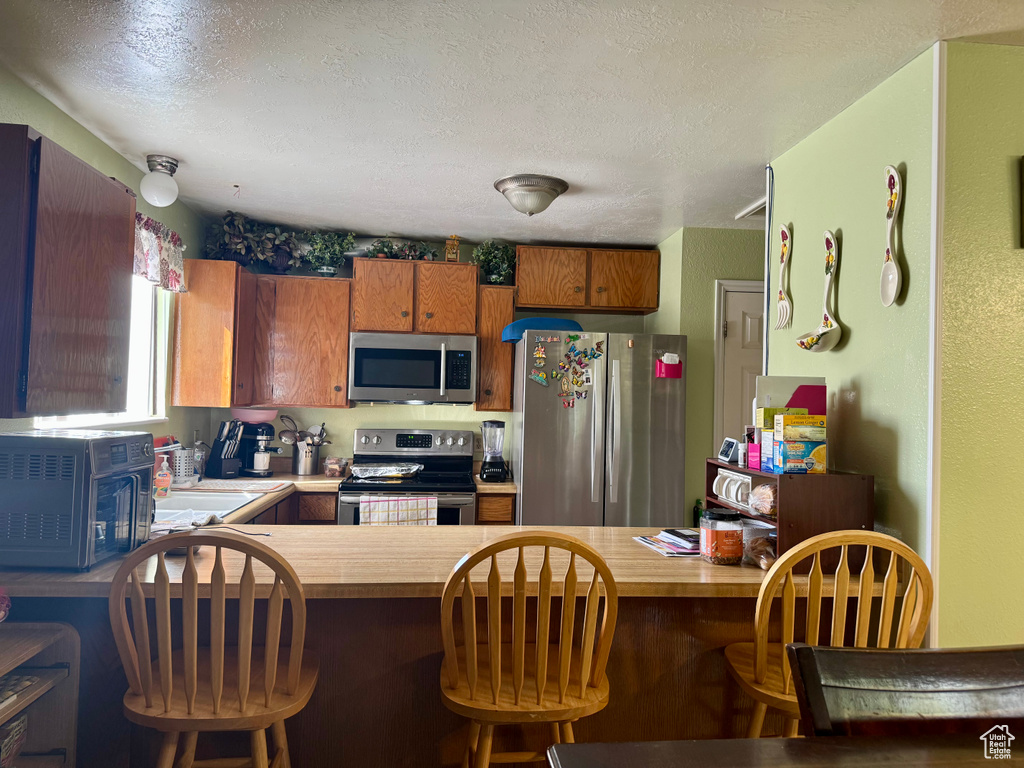 Kitchen with stainless steel appliances, a peninsula, a textured ceiling, and butcher block counters