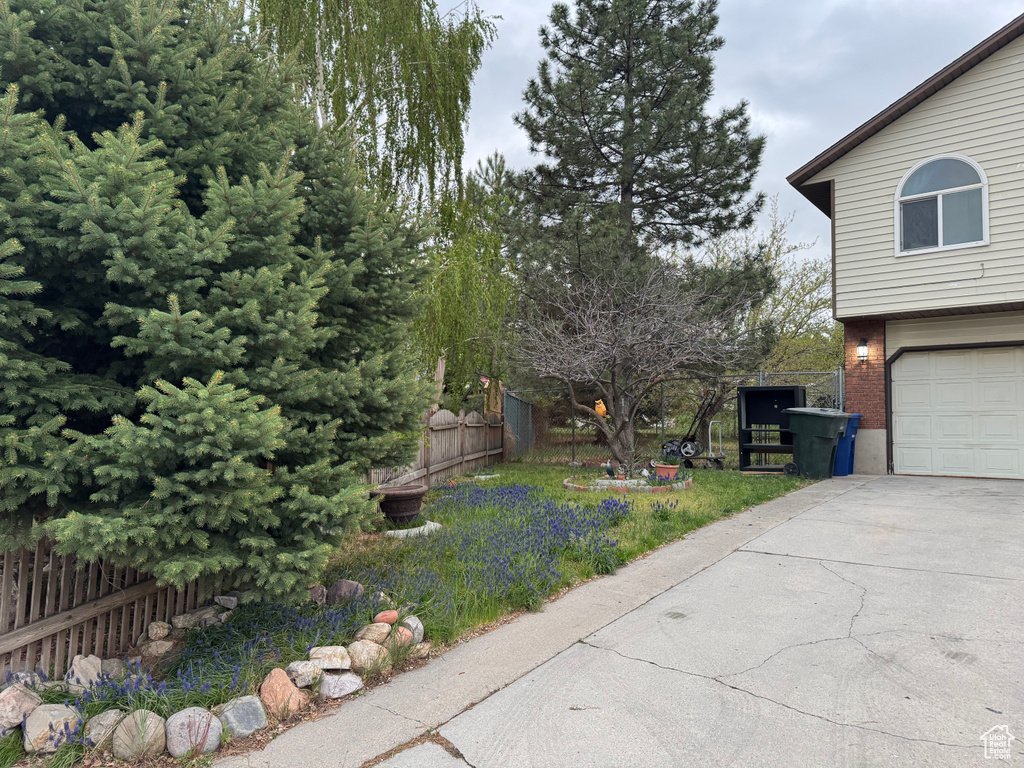 View of yard with fence, a garage, and concrete driveway
