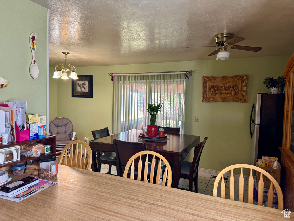 Dining area with a ceiling fan, a chandelier, tile patterned floors, a textured ceiling, and baseboards