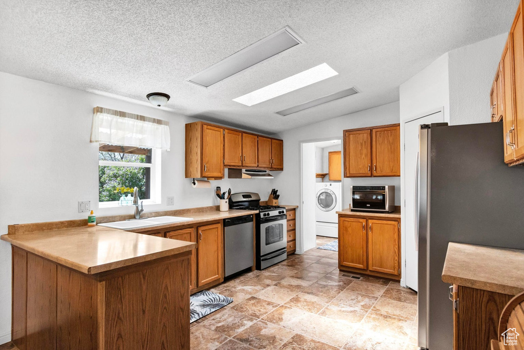 Kitchen with a sink, brown cabinetry, washer / dryer, and appliances with stainless steel finishes