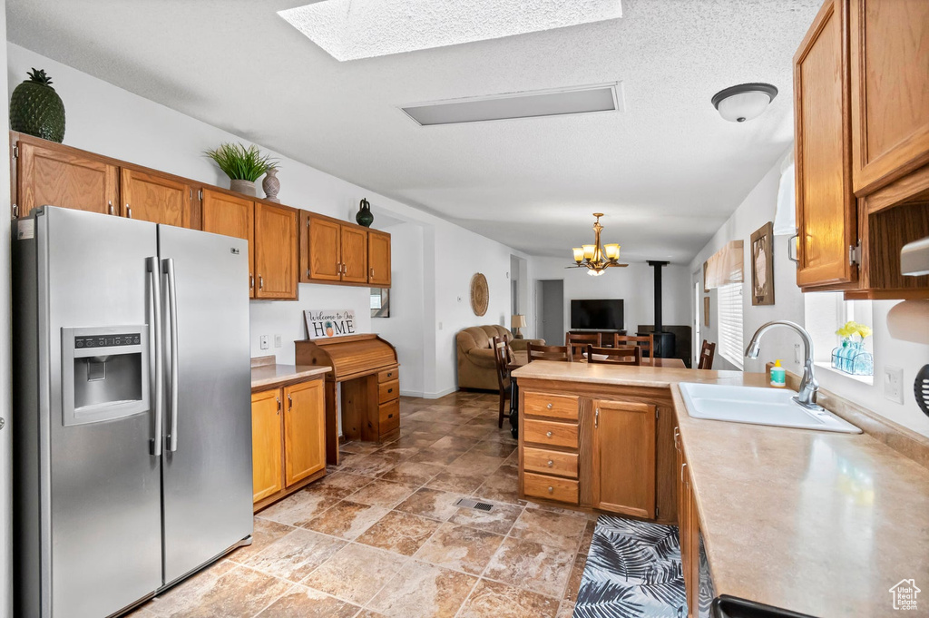 Kitchen featuring a sink, a peninsula, brown cabinets, stainless steel refrigerator with ice dispenser, and light countertops