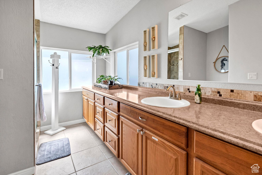 Bathroom with a shower stall, visible vents, double vanity, and a sink