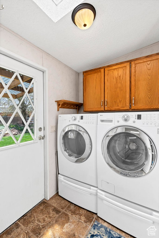 Clothes washing area with washing machine and dryer, a textured ceiling, stone finish floor, cabinet space, and a skylight