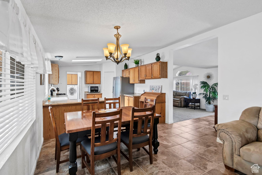 Dining space featuring lofted ceiling, a textured ceiling, an inviting chandelier, tile patterned floors, and washer / dryer