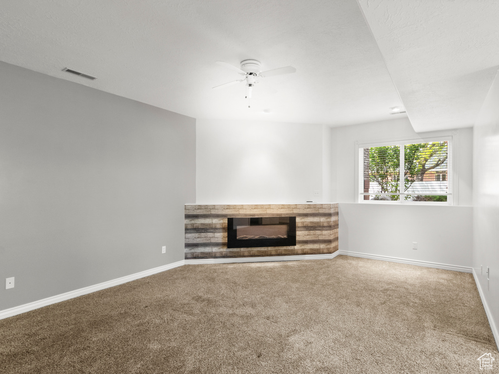Unfurnished living room featuring baseboards, a glass covered fireplace, ceiling fan, and carpet floors